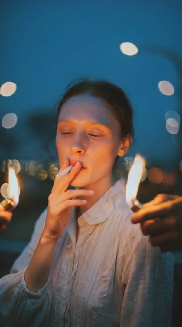 Vertical night portrait of a woman lit by small flames with drifting smoke